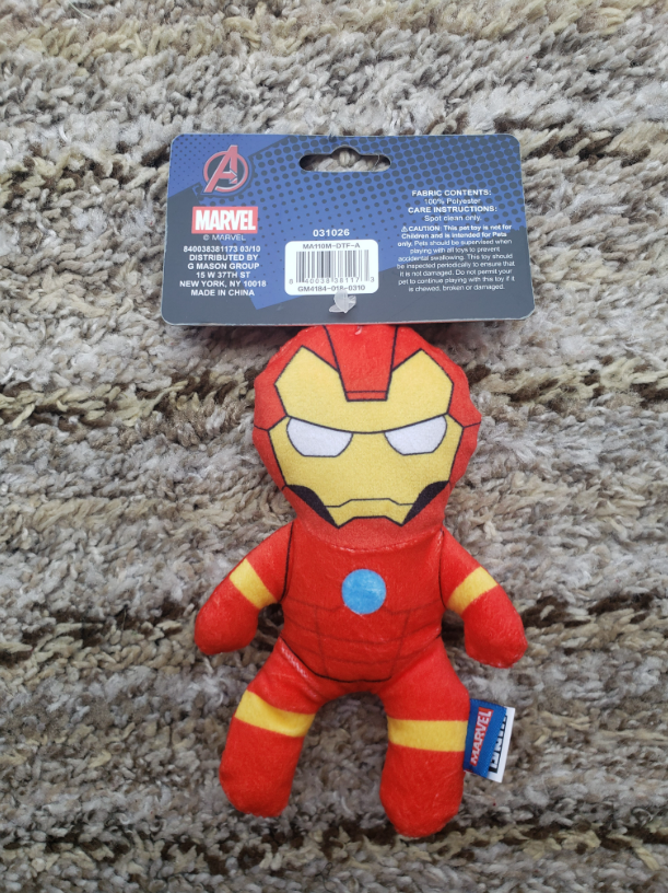 A small Marvel Avengers Iron Man plush toy in its retail packaging, placed on a textured beige carpet. The packaging card features the Marvel logo and the Avengers logo.