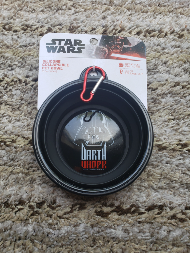 Star Wars Darth Vader silicone collapsible pet bowl in its retail packaging, placed on a beige carpet. The packaging features the Star Wars logo and a red carabiner clip.